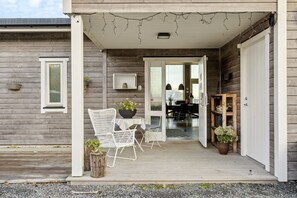 Una casa di legno con un portico, un tavolo con sedie e una zona pranzo visibile attraverso una porta aperta.