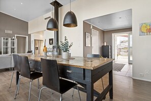 Une cuisine moderne avec un îlot central en bois, des chaises noires, des luminaires suspendus et une vue sur l’extérieur.