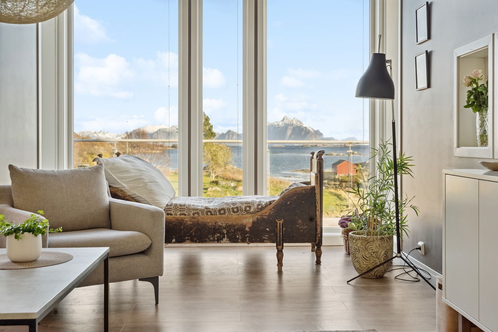 A room with a bed, a sofa, a table, and a view of a lake and mountains.