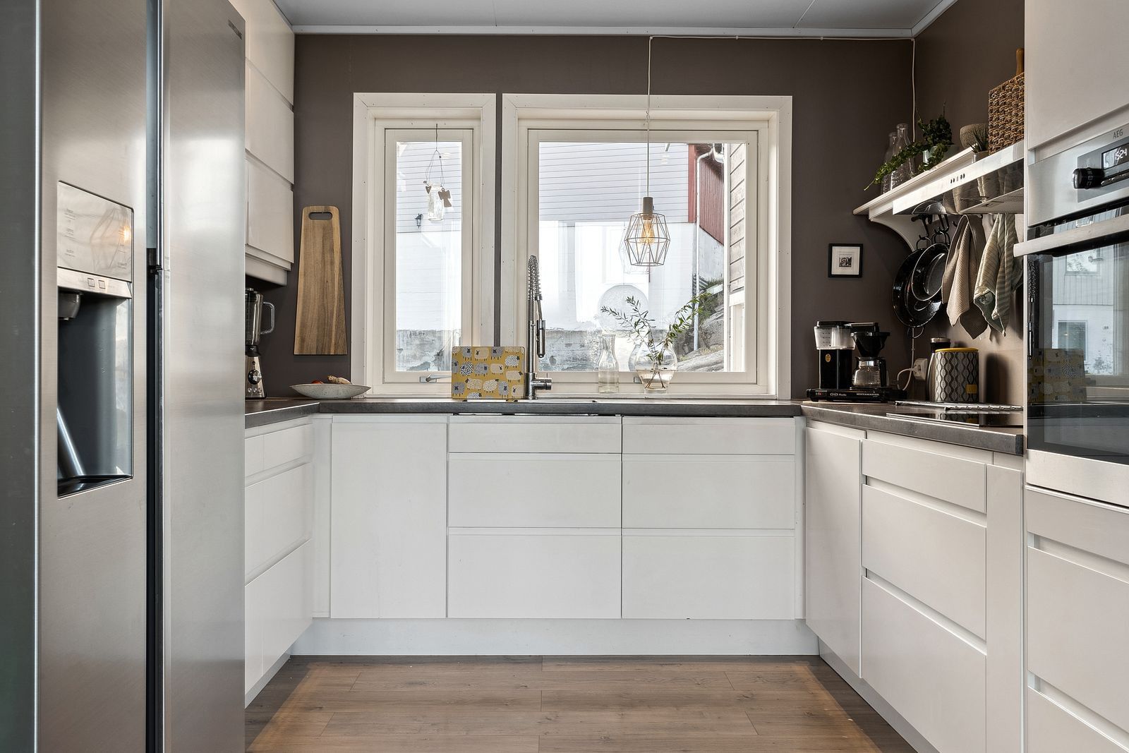 A modern kitchen with white cabinetry, a double sink, and a window with a view.