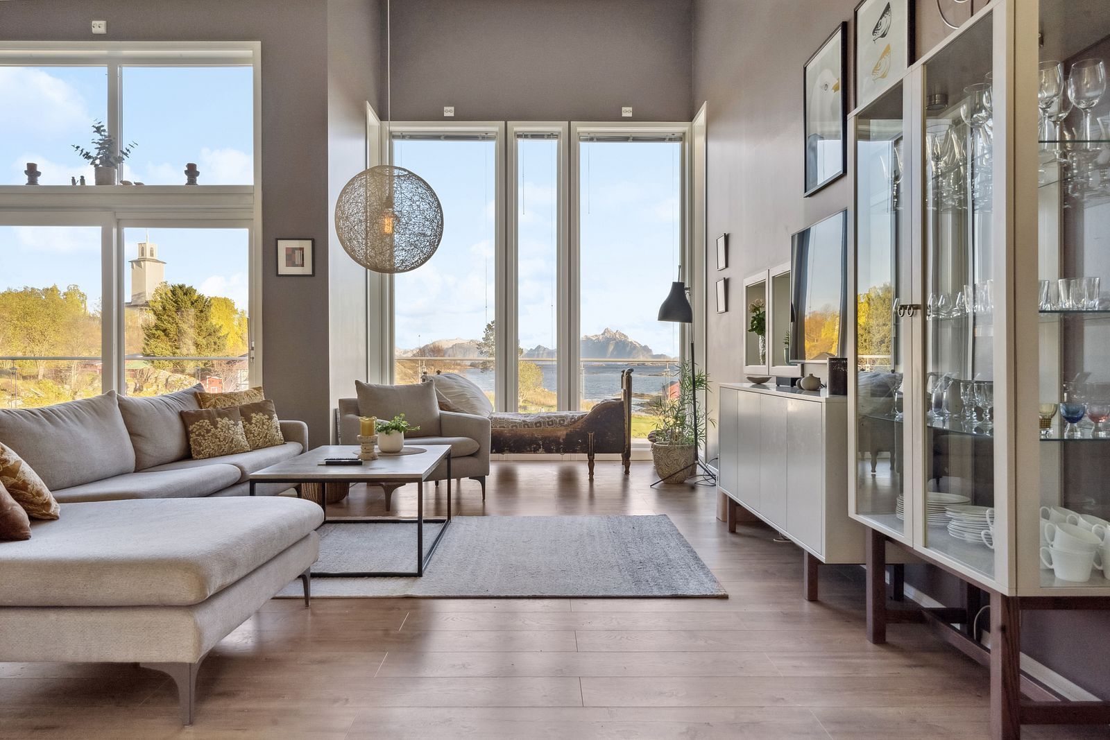 A spacious living room with a sofa, coffee table, and a view of a lake through large windows.