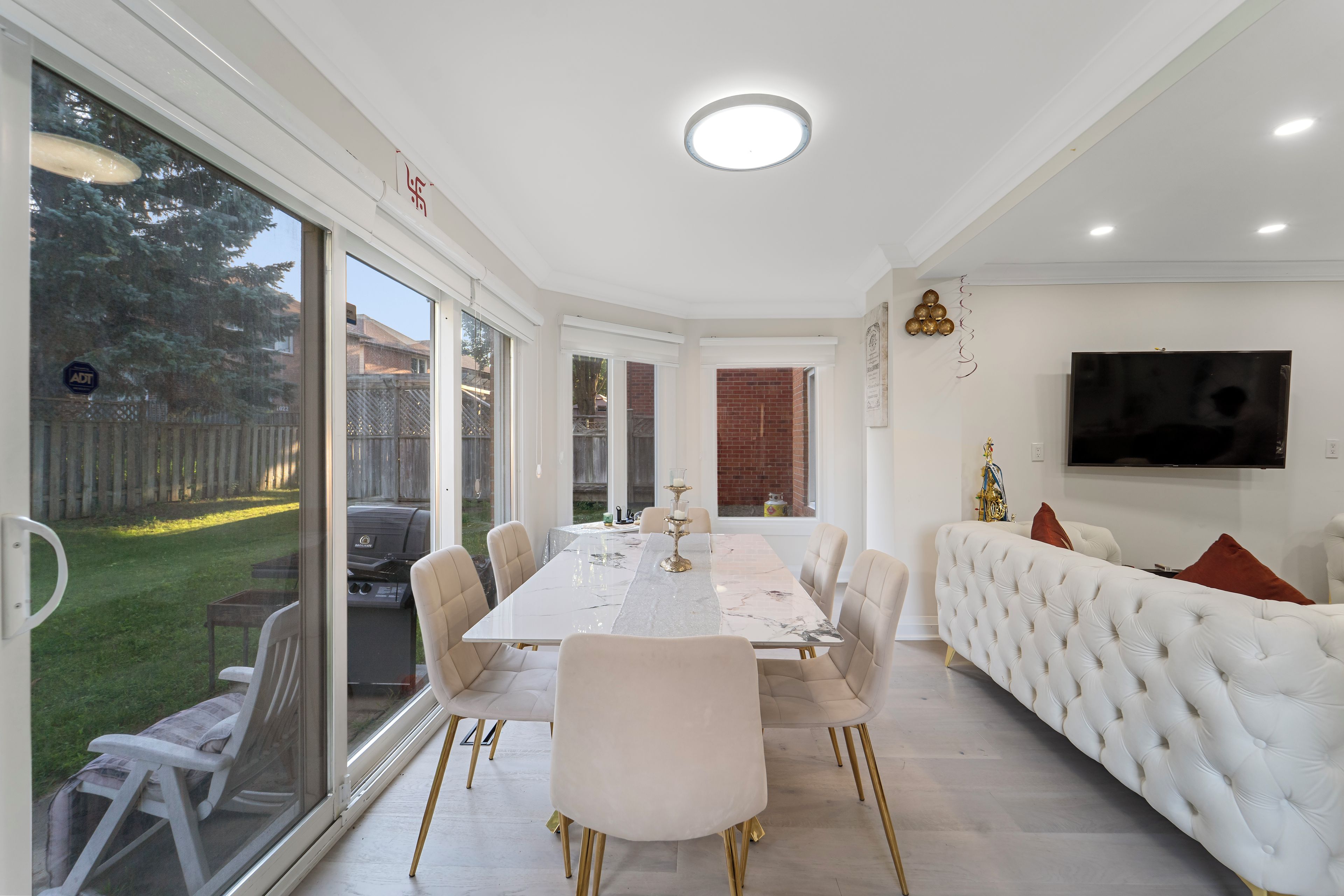 A dining area with a white table and chairs, a sofa, and a TV on the wall.