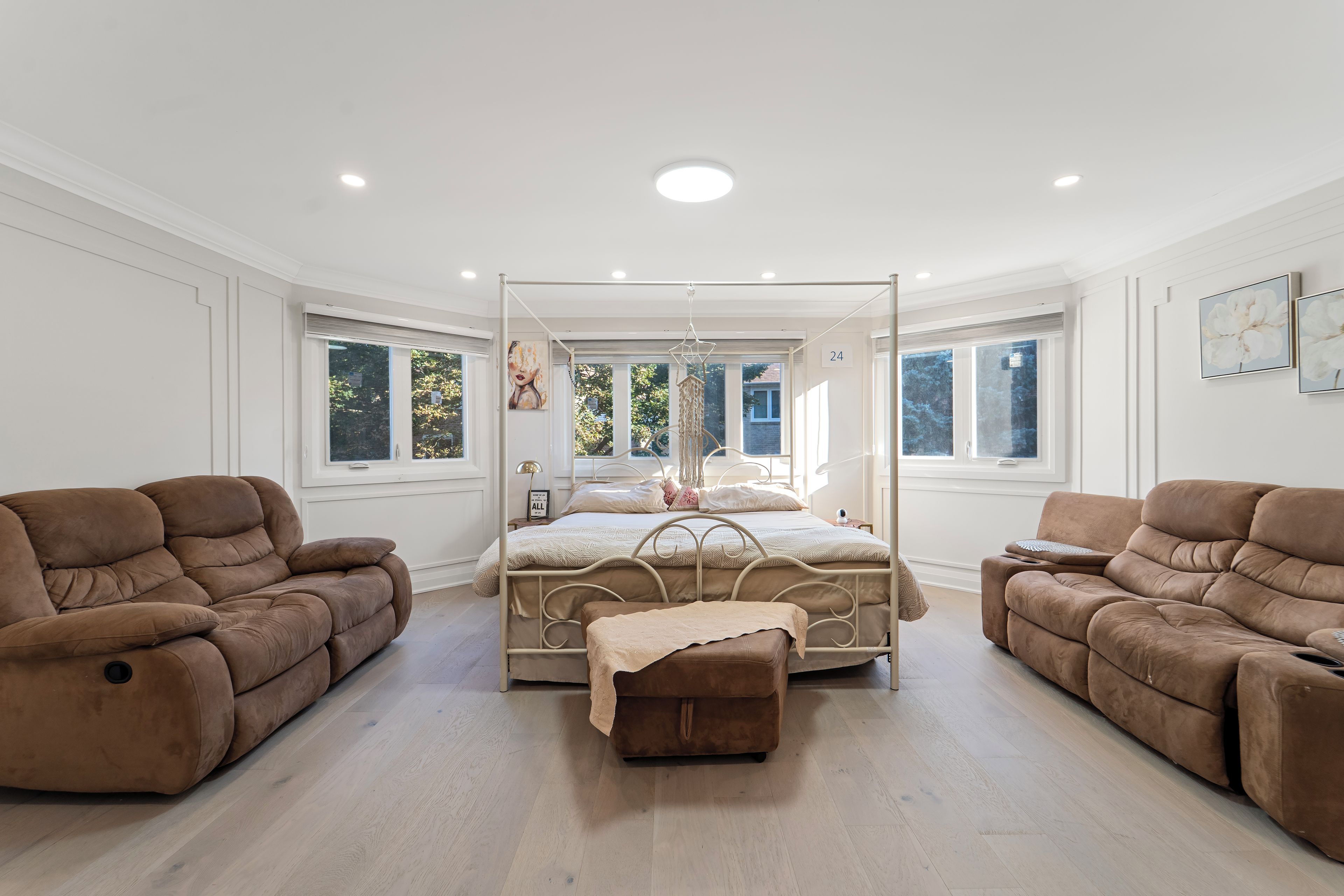 A spacious bedroom with a four-poster bed, two sofas, and large windows.
