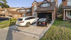 A residential driveway with two cars parked, a brick house with a garage, and a clear sky.