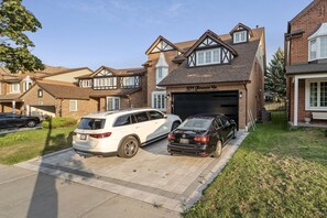 A residential driveway with two cars parked, a brick house with a garage, and a clear sky.