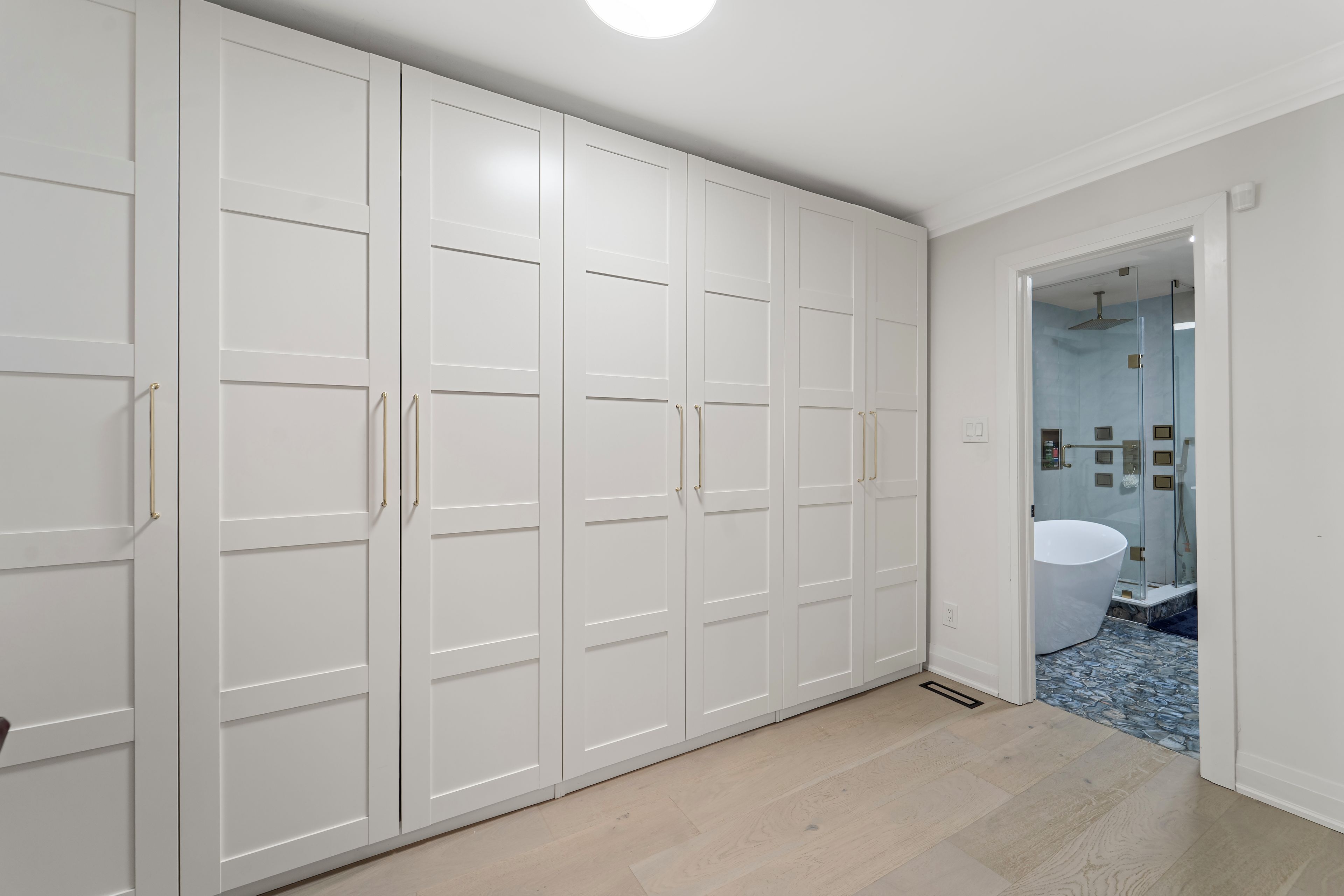 Un dressing avec des portes et des poignées blanches, une salle de bain avec un lavabo et une douche blancs, et un sol carrelé.