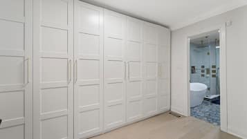 Un dressing avec des portes et des poignées blanches, une salle de bain avec un lavabo et une douche blancs, et un sol carrelé.