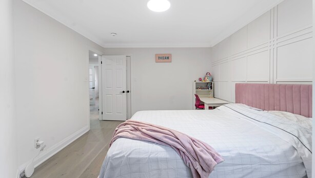 A bedroom with a bed, a pink headboard, a white door, and a wall-mounted sign.