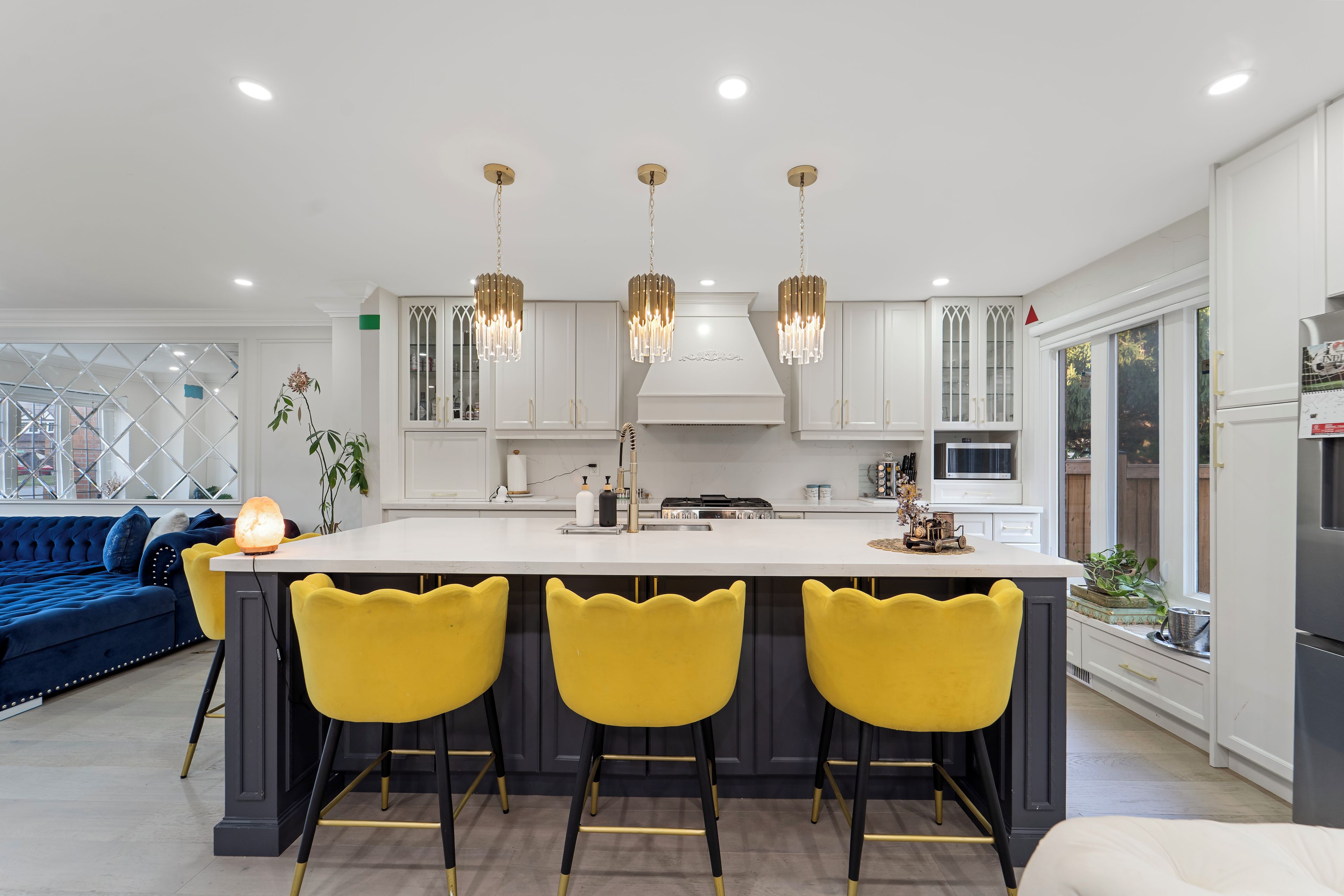 A modern kitchen with a central island, bar stools, pendant lights, and a built-in oven.
