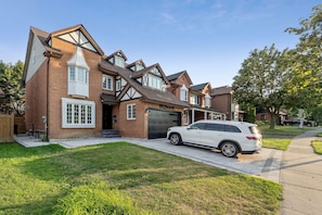 A two-story house with a garage, a driveway, and a white SUV parked in front.