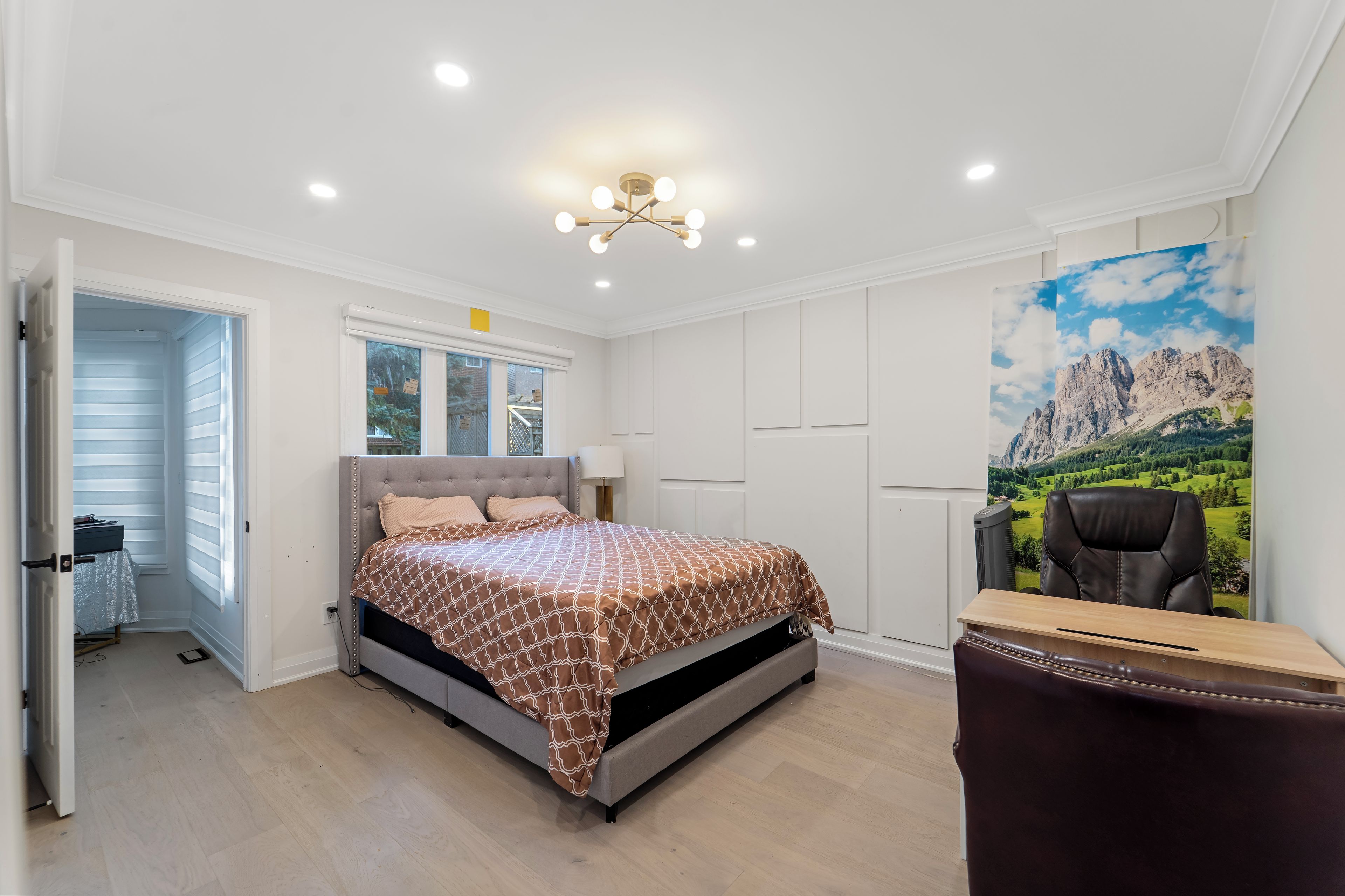 A bedroom with a bed, a desk, a chair, and a large window with a mountain view.