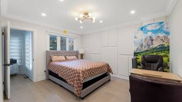 A bedroom with a bed, a desk, a chair, and a large window with a mountain view.