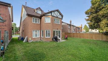 A two-story brick house with a fenced backyard, a barbecue grill, and a wooden deck.