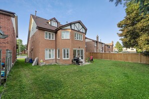 A two-story brick house with a fenced backyard, a barbecue grill, and a wooden deck.