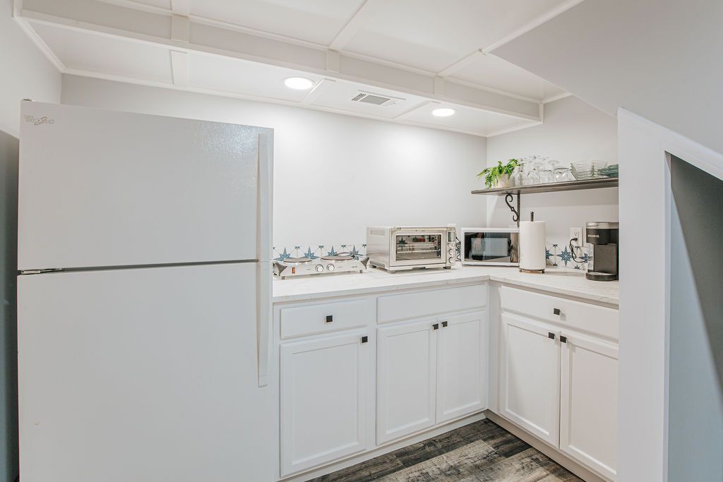 A kitchen with white cabinets, a refrigerator, a microwave, a coffee maker, and a shelf with plants.