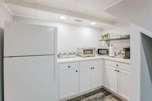 A kitchen with white cabinets, a refrigerator, a microwave, a coffee maker, and a shelf with plants.