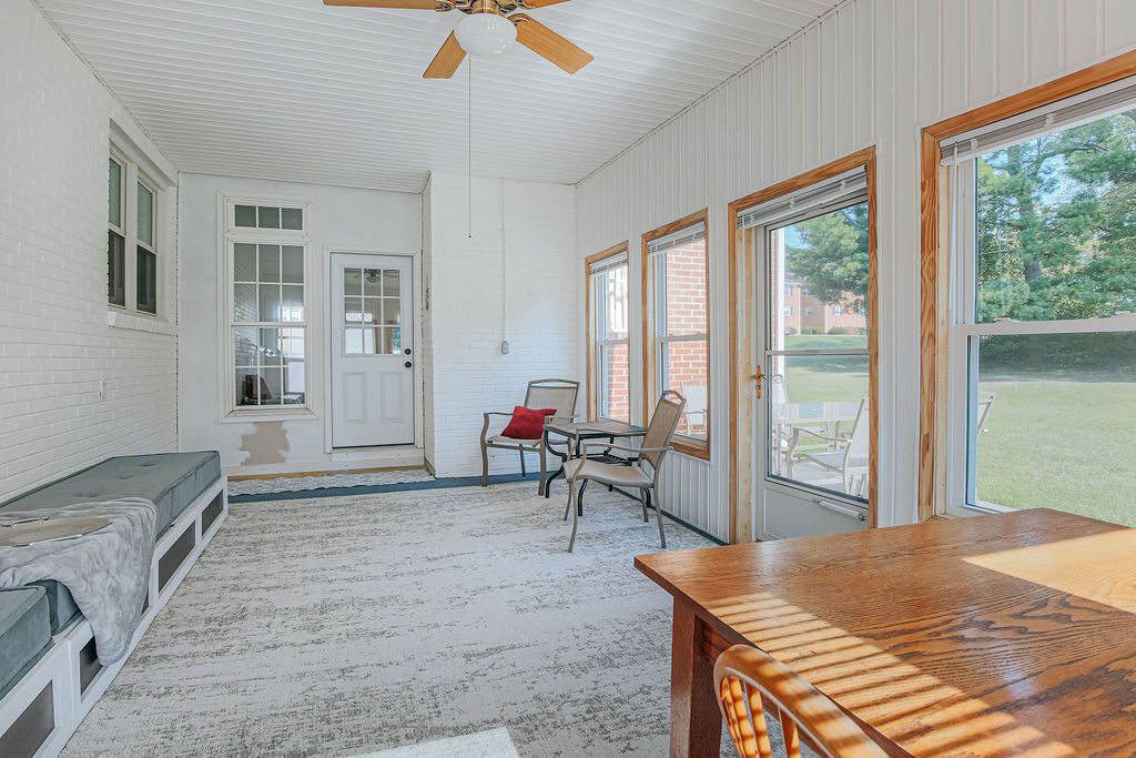Quarto com ventilador de teto, um banco, uma mesa e vista para o exterior.