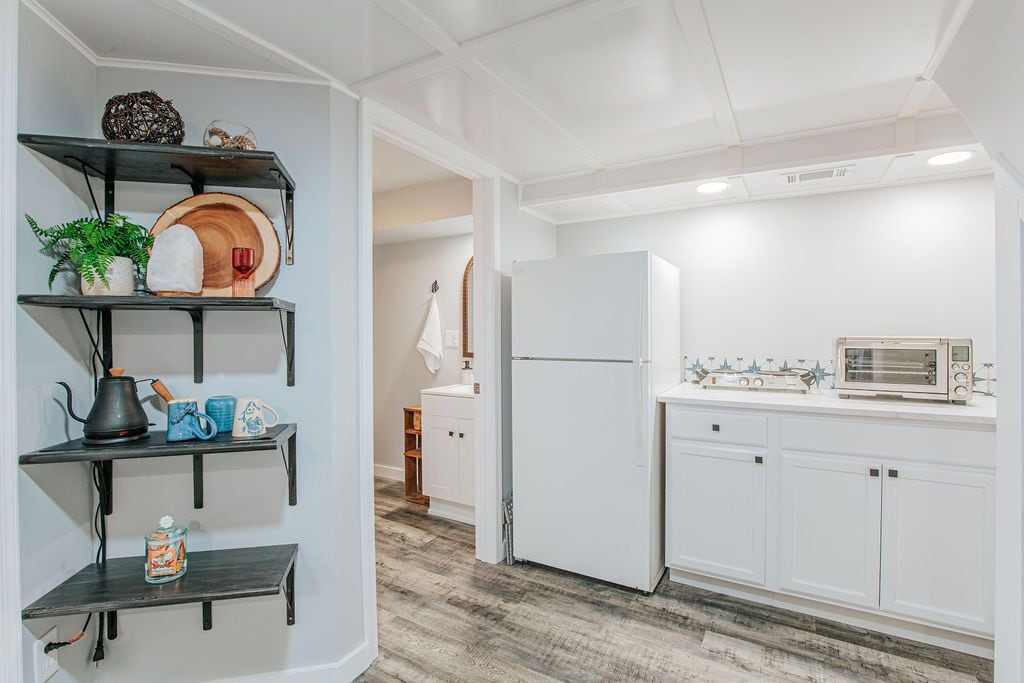 A kitchen with white cabinets, a white refrigerator, a microwave, and a shelf with various items.