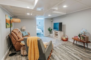 Una sala moderna con sofá, sillón, televisor y estantería.