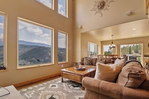 A spacious living room with large windows offering a mountain view, a cozy sofa, and a dining area. - Secluded private home with incredible views (Silverthorne)