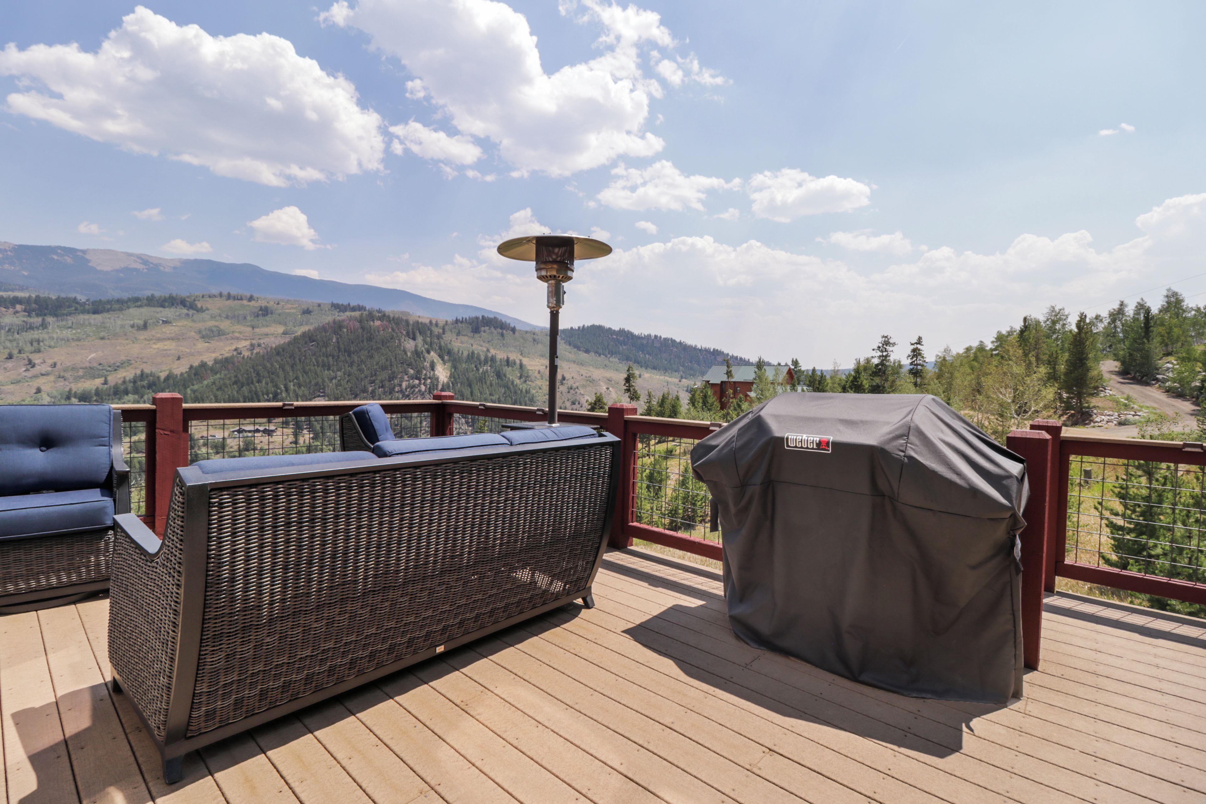 A deck with outdoor furniture, a covered grill, and a view of a mountainous landscape.