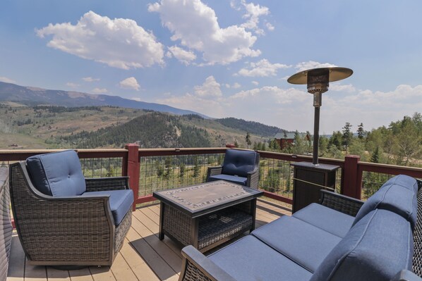 Une terrasse dotée de meubles en osier et d’une table, offrant une vue sur un paysage montagneux.