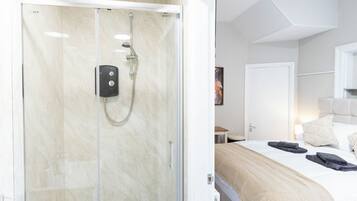 A hotel room with a shower, bed, bedside table, and a door.