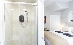 Et hotelværelse med bruser, seng, natbord og dør.