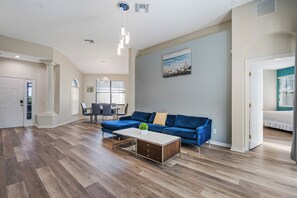 A spacious living area with a blue sofa, a coffee table, and a dining table with chairs. - Bright & Spacious 6BR Near Disney w/Pool (Davenport)