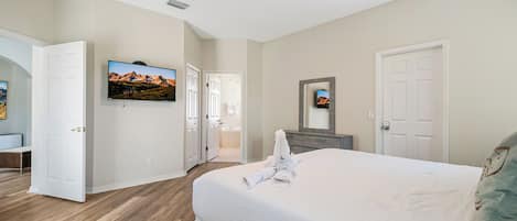 A hotel room with a large bed, a television, a bathroom, and a door leading to another room.