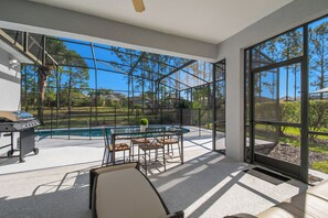 A modern outdoor patio with a glass enclosure, a pool, and a barbecue grill. - Bright & Spacious 6BR Near Disney w/Pool (Davenport)