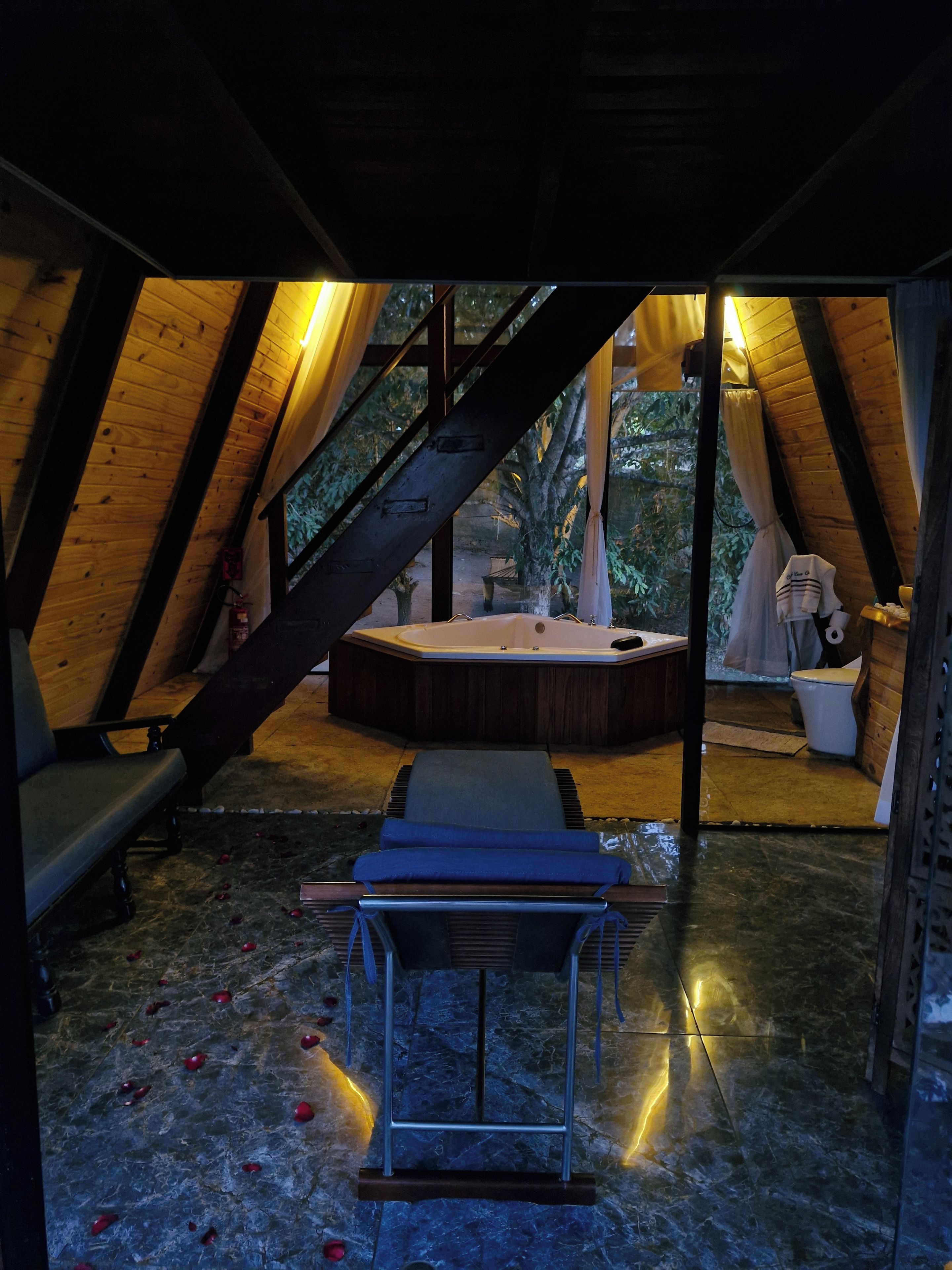 Área de spa com hidromassagem, bancos de madeira e piso de pedra.