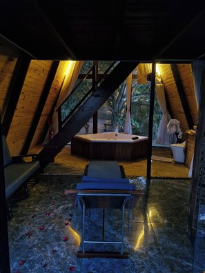 Un espacio de spa con una bañera de hidromasaje, bancos de madera y suelo de piedra.