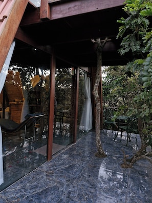 A covered outdoor area with a glass partition, a metal table, and chairs.