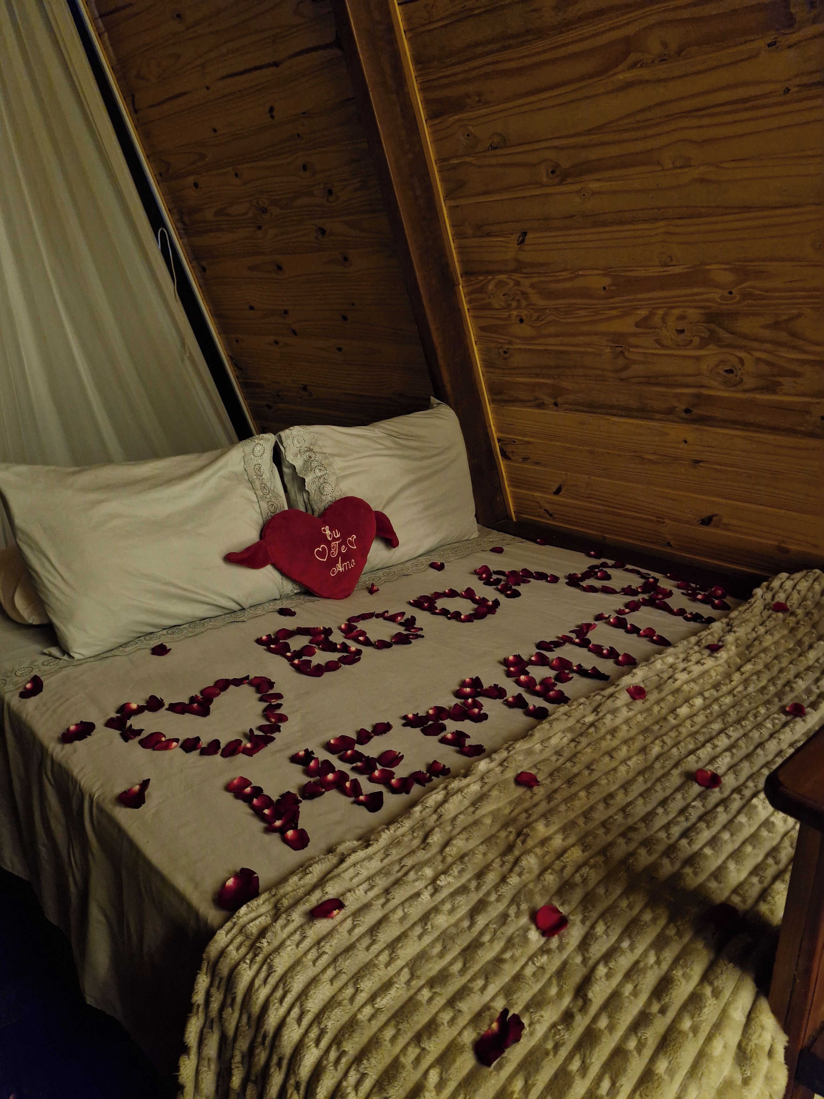 A bed with a heart-shaped arrangement of rose petals spelling 'Love' and a red heart-shaped pillow with the text 'You are my love' on it.