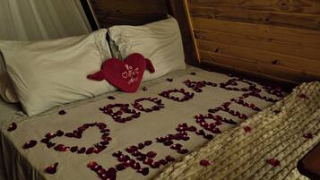 A bed with a heart-shaped arrangement of rose petals spelling 'Love' and a red heart-shaped pillow with the text 'You are my love' on it.