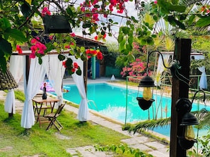 A poolside area with a wooden table and chairs, a hanging light fixture, and a white canopy.