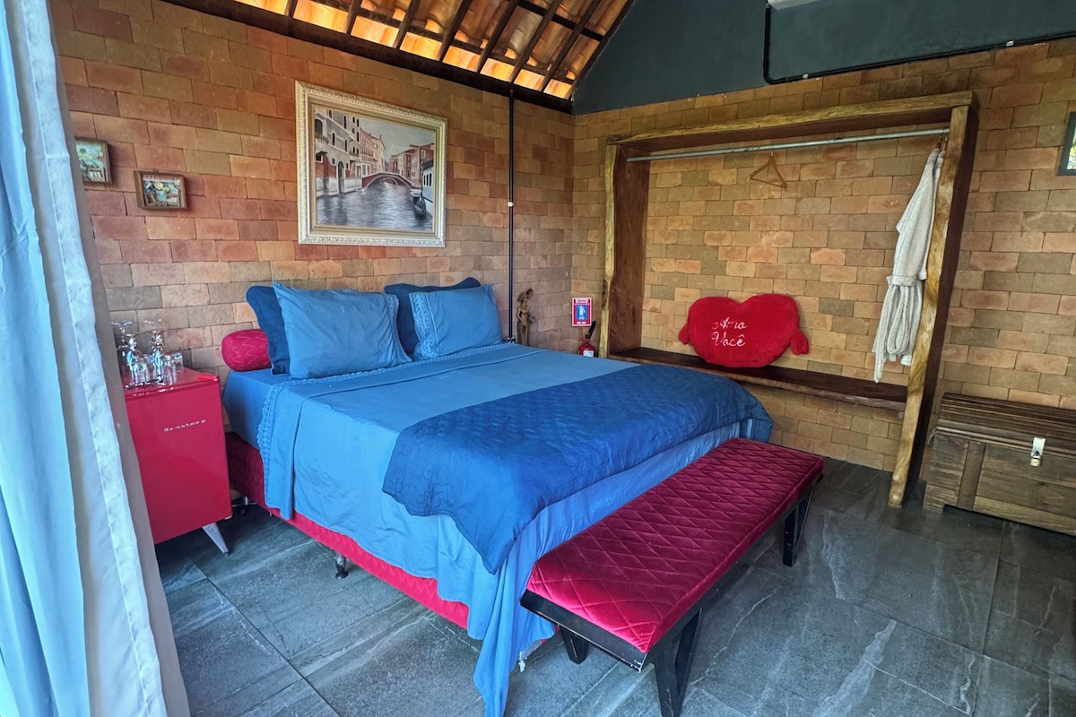 Una habitación con cama, una mesita de noche roja, aire acondicionado instalado en la pared y un cuadro enmarcado.