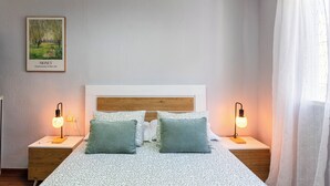 Une chambre à coucher avec un lit, deux lampes de chevet, un tableau encadré et une fenêtre avec des rideaux.
