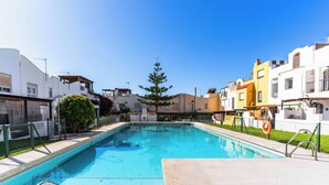 Une piscine à l’eau d’un bleu limpide, entourée d’une clôture et jouxtant des bâtiments dotés de balcons et de fenêtres.