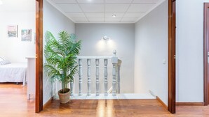 Un couloir avec un plancher en bois, un escalier dot é d’une balustrade blanche et une plante en pot.