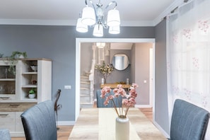 A dining area with a table, chairs, a vase with flowers, and a staircase leading to a different room.
