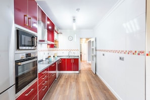 A modern kitchen with red cabinetry, stainless steel appliances, and a tiled backsplash.