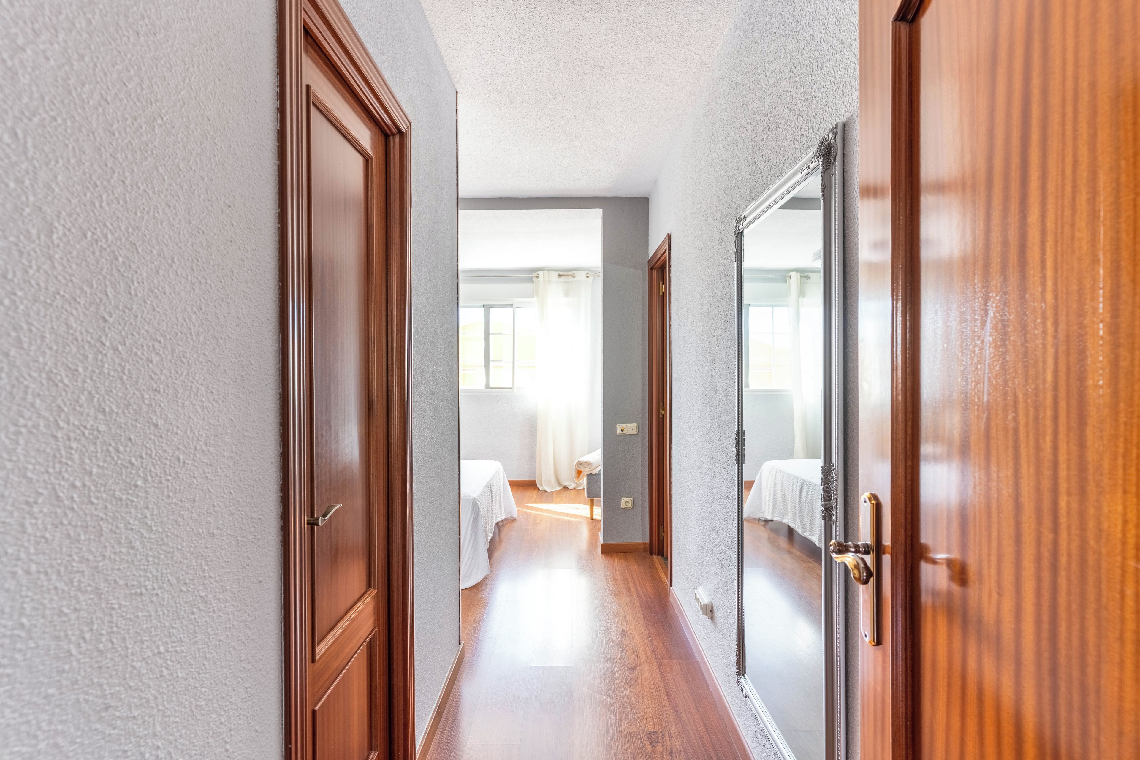Un pasillo con puertas de madera y una cama con colcha blanca al fondo.