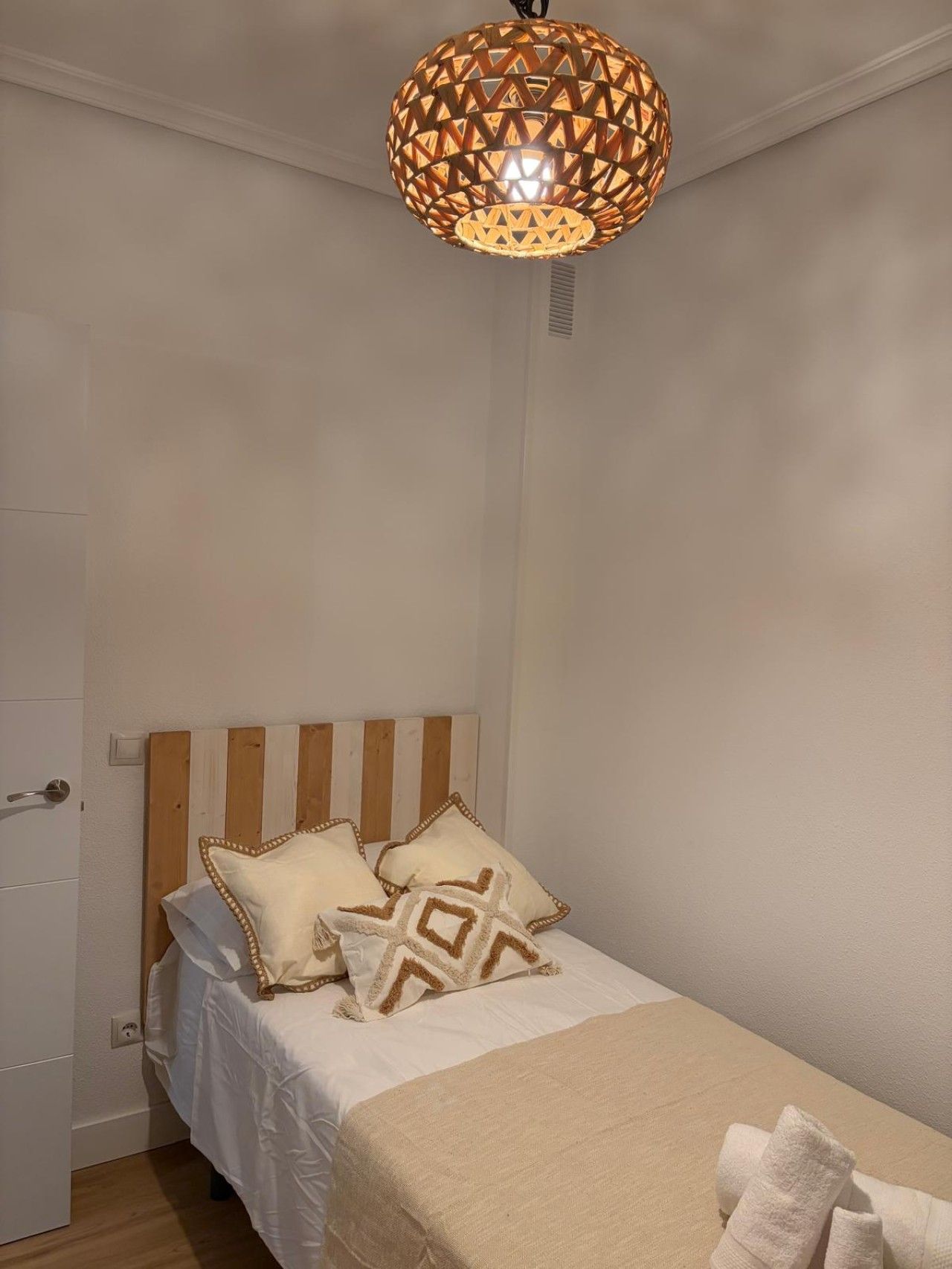 Un dormitorio con cabecera de madera, cama con ropa de cama blanca, dos almohadas decorativas y una lámpara colgante.
