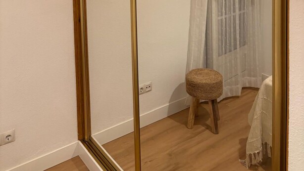 A room with a large mirror, a wooden stool, a window with sheer curtains, and a white tablecloth. - Spacious Apartment in Moncloa, Madrid (Madrid)