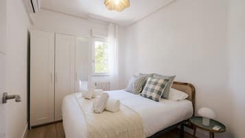 Un dormitorio con cama, mesita de noche, armario y ventana.