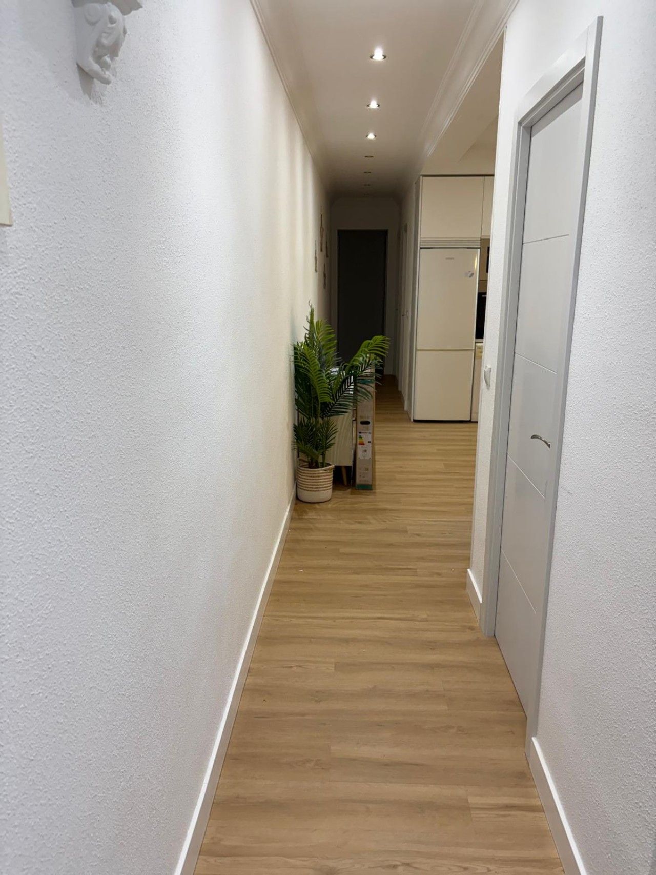 Un pasillo con paredes blancas, piso de madera y una puerta al final.