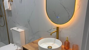 A modern bathroom with a marble wall, a white toilet, a wooden vanity with a round sink, and a gold faucet. - Spacious Apartment in Moncloa, Madrid (Madrid)