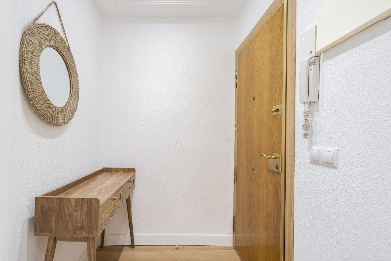 Un pasillo con un banco de madera, una puerta de madera y una lámpara de pared.